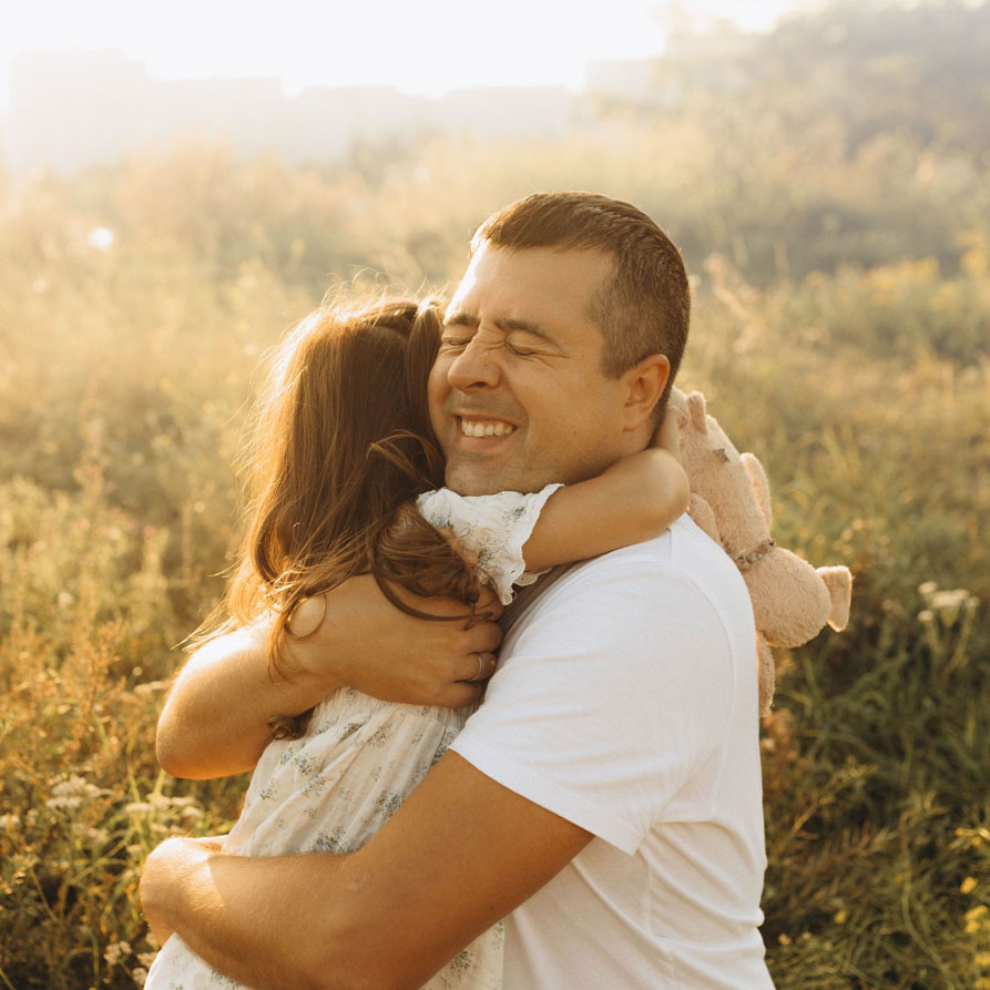A dad hugging his daughter in a sunlit field